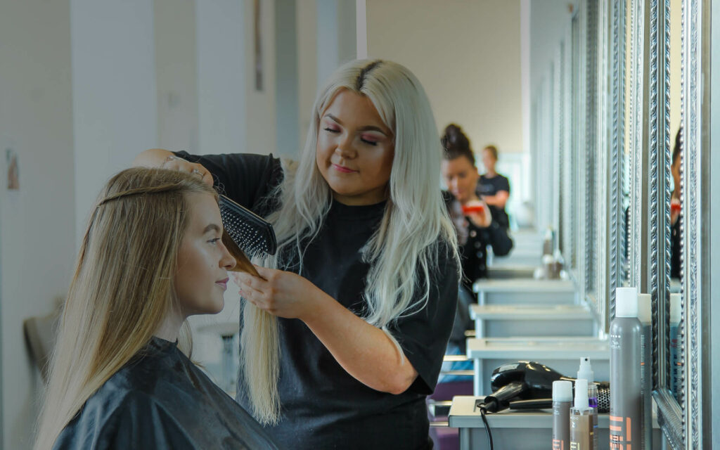 Hairdressing student learning to style a model's long hair in hairdressing studio