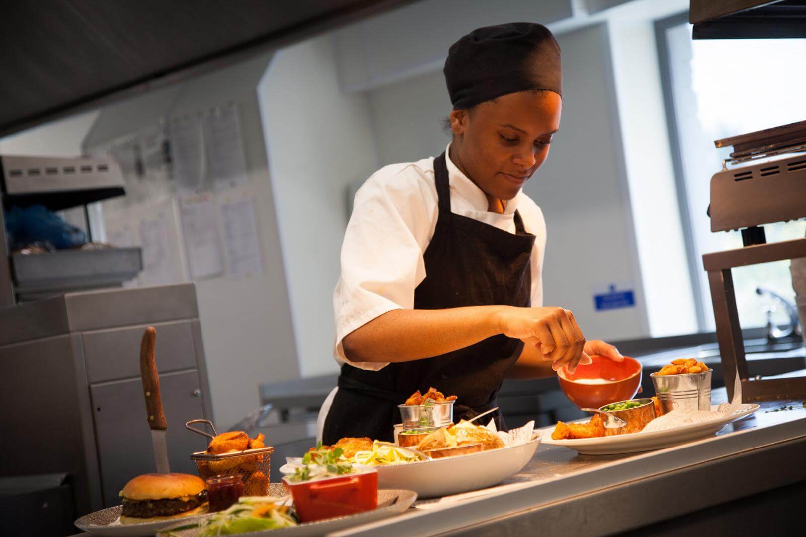 Hospitality and Catering student in chef overalls plating up meals in kitchen
