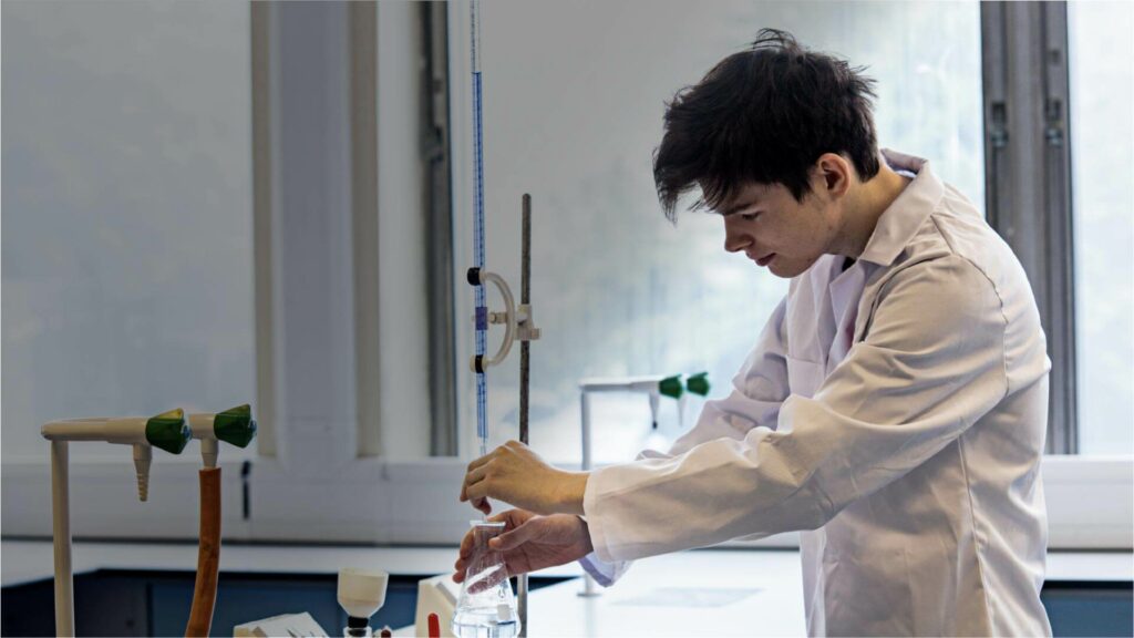 Student wearing a white lab coat doing a science experiment with liquid in a flask and a thermometer