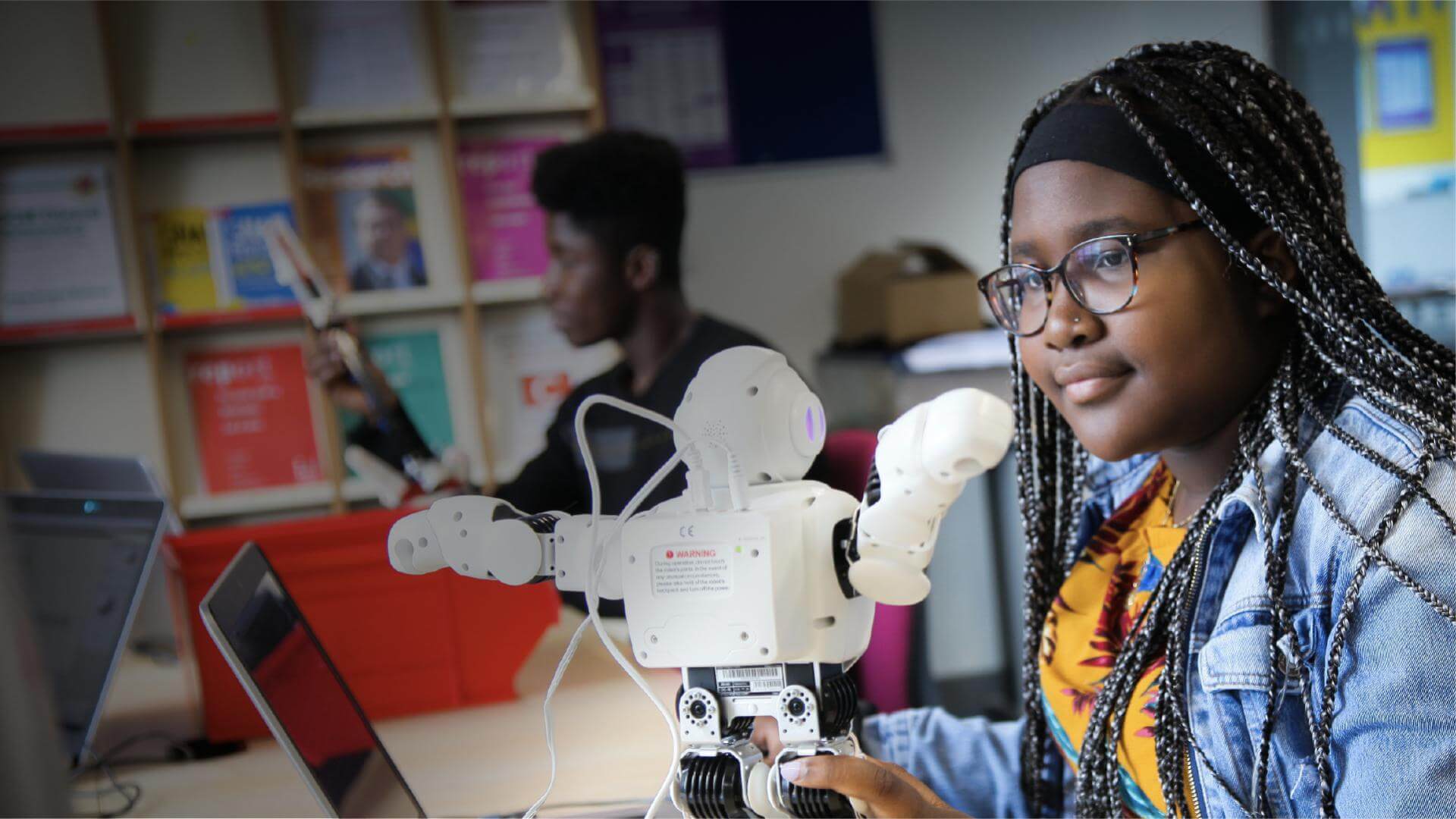 Student sat by laptop which is wired to a mini robot