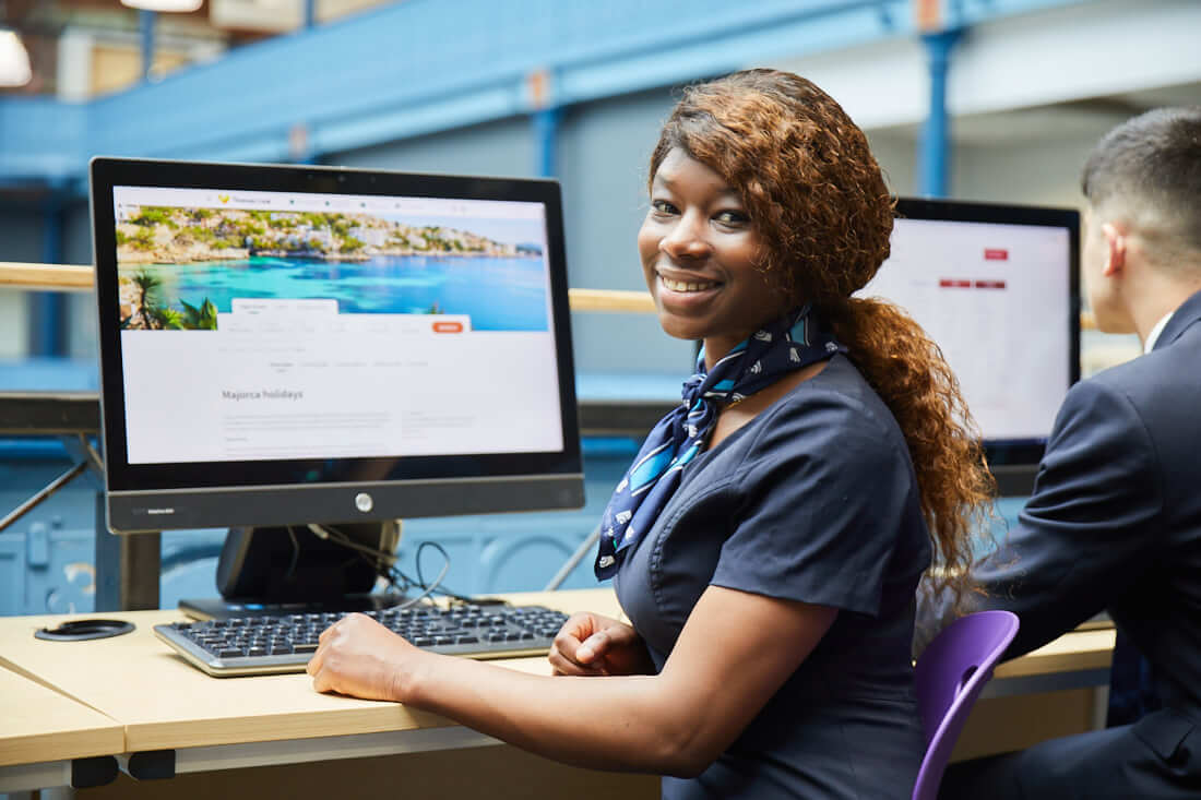 Travel and tourism student wearing uniform and neckerchief sat in front of computer learning to book holidays