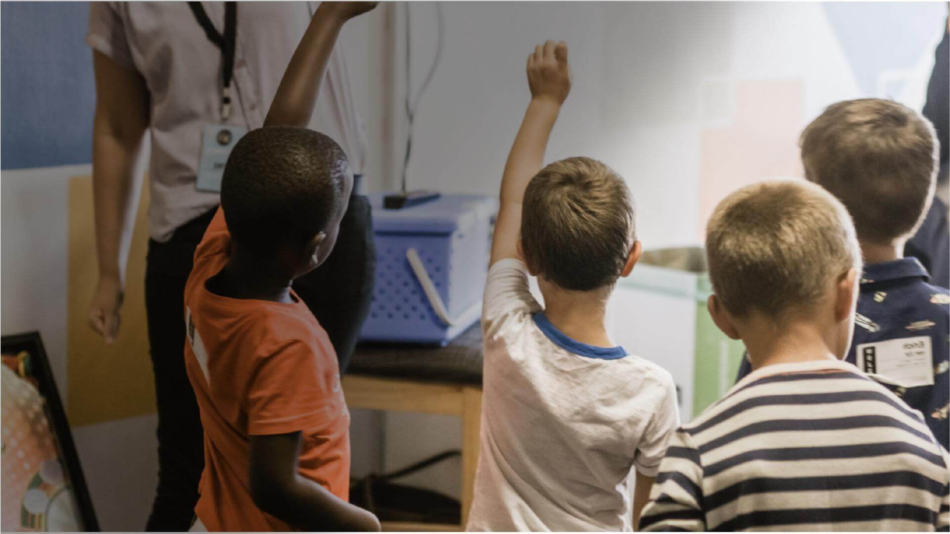 Class of children raising their hand to answer the teacher