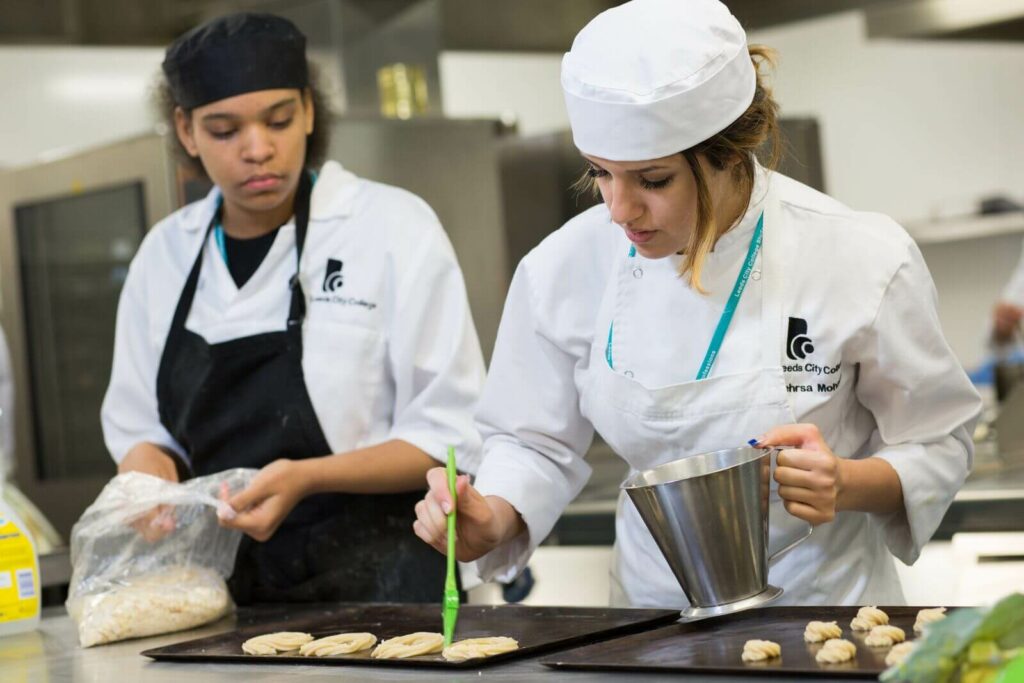 Hospitality and Catering students in chef overalls adding patisseries to baking trays