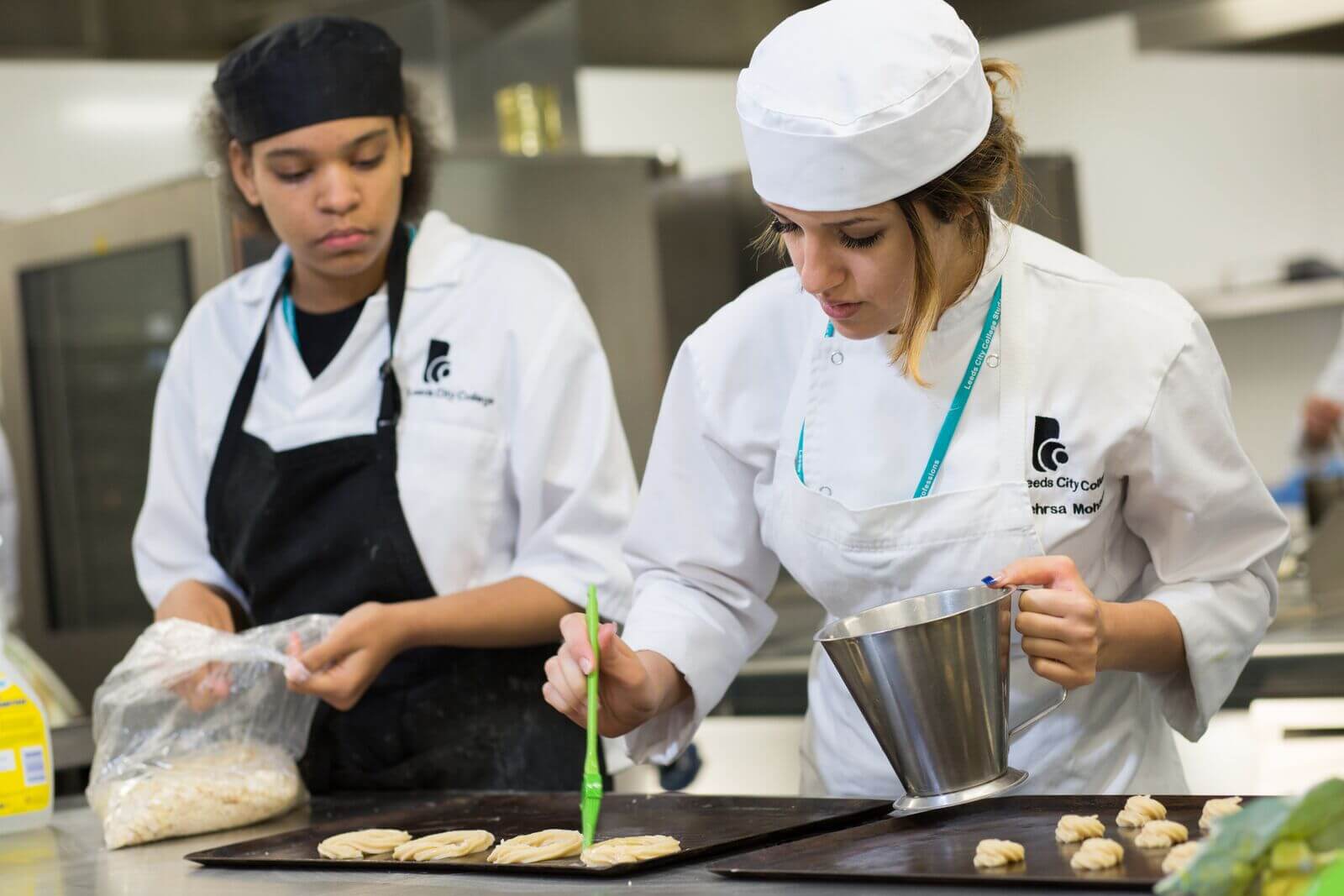 Hospitality and Catering students in chef overalls adding patisseries to baking trays