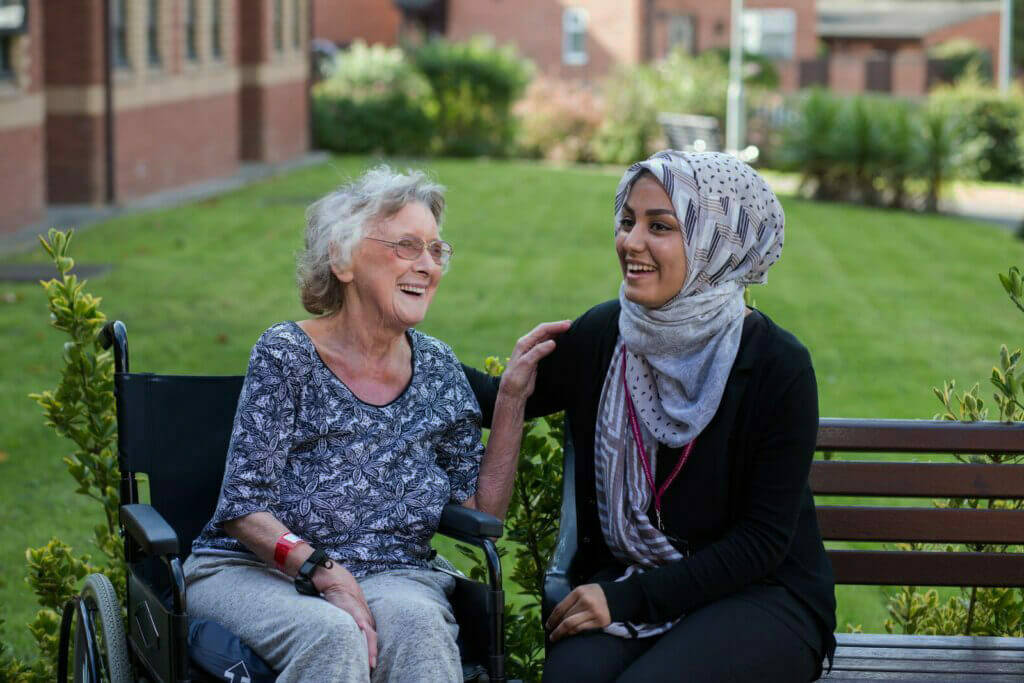 Social care worker looking after an elderly woman, sat outside on a summers day