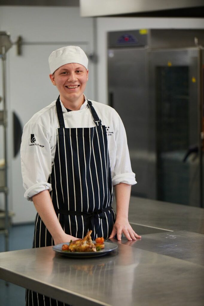 Travel and Food student in the kitchens presenting a plate of roast chicken with salad
