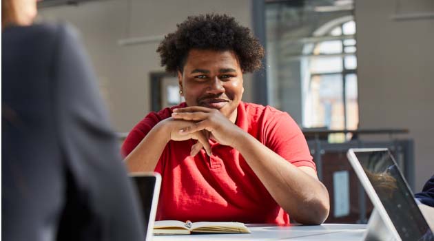 Student sat at a desk smiling with hands clasped together