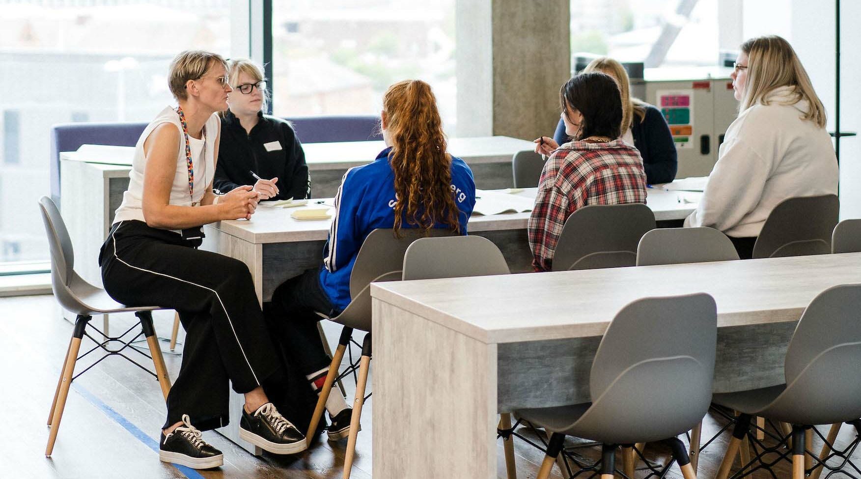 Students and teacher sat around classroom table having a discussion