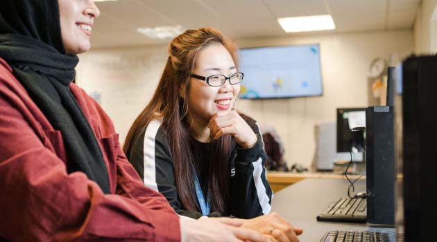 Two adults sat in a classroom looking at a computer screen together