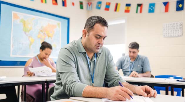 Three adults sat in a classroom looking down and studying
