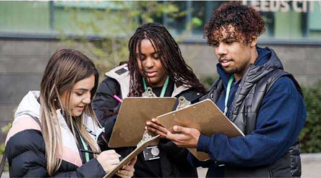 Three students outside Leeds City College with clipboards and pens wearing college lanyards