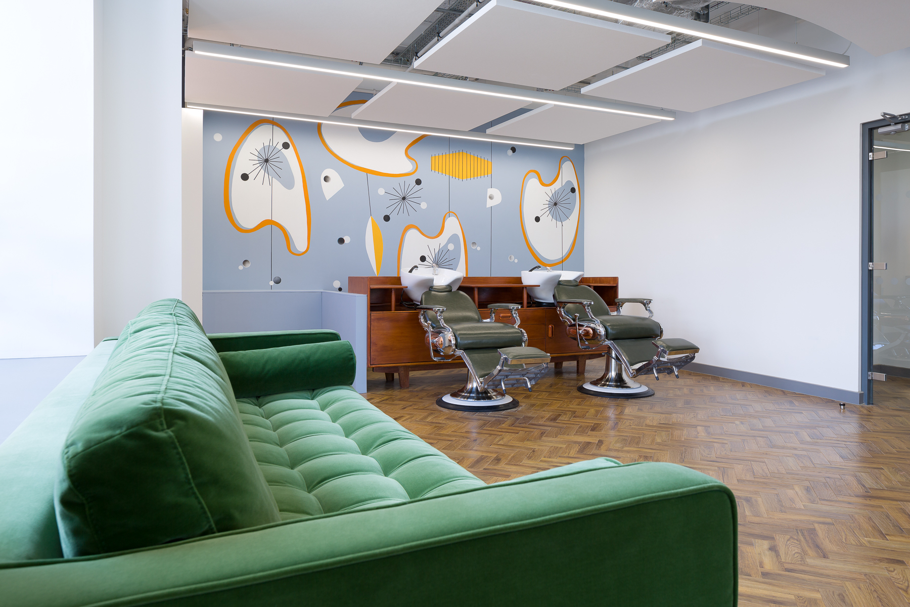 Two hair washing basins with chairs, and a green sofa in Printworks Salon & Spa