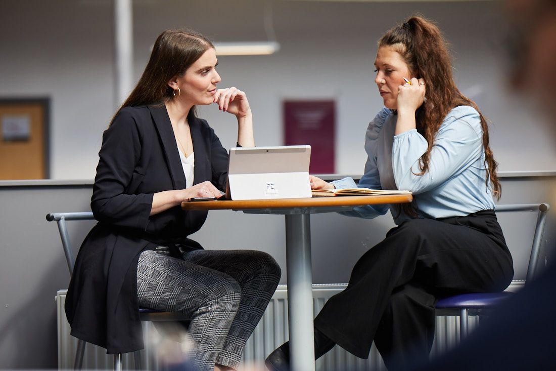 Two students sat at a small round table talking to each other
