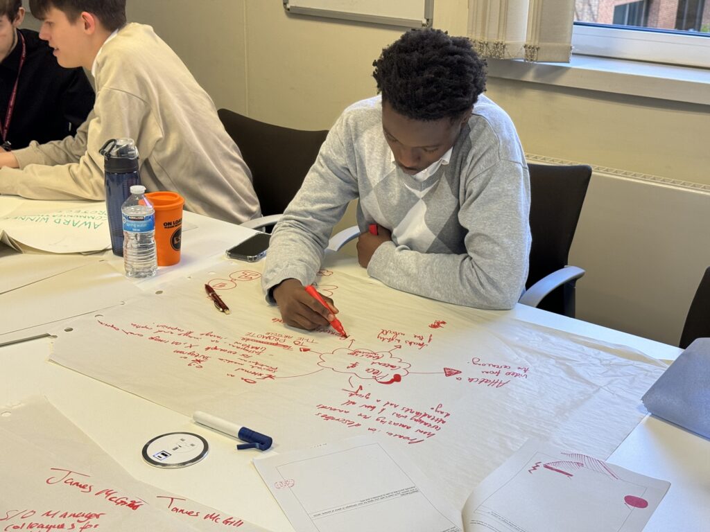 Student sat at a desk brainstorming ideas with red pen on a large piece of paper