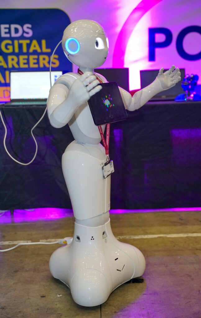 A robot stands before a sign displaying the text "Leeds Digital Careers Fair"