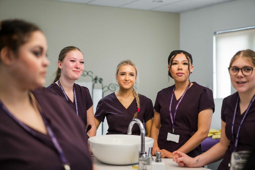 A group of 5 hair and beauty students stood for a photo wearing their uniform smiling looking toward the camera in the salon