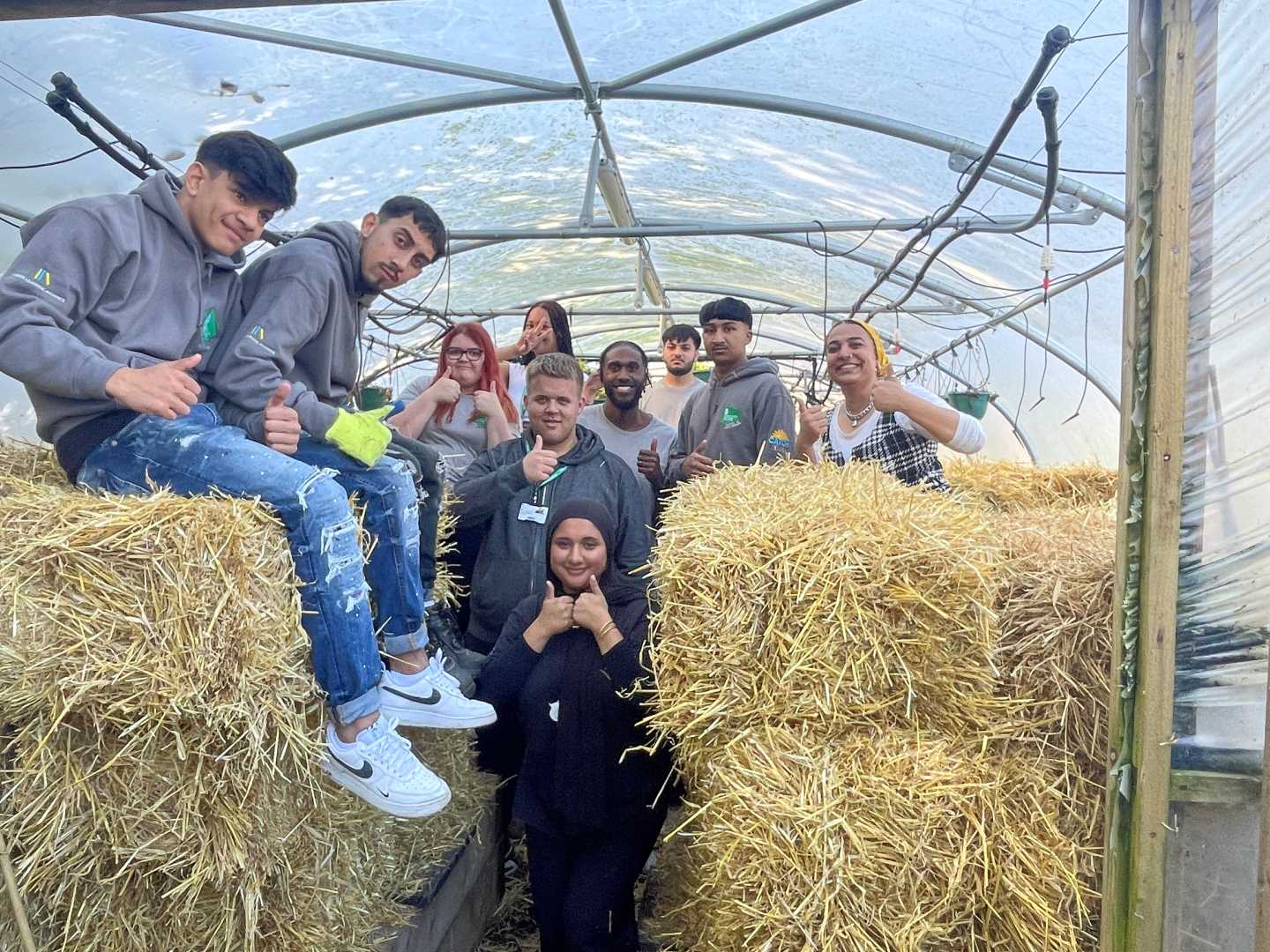 A group of apprenticeship students out helping on a farm posing for a photo next to hay bales