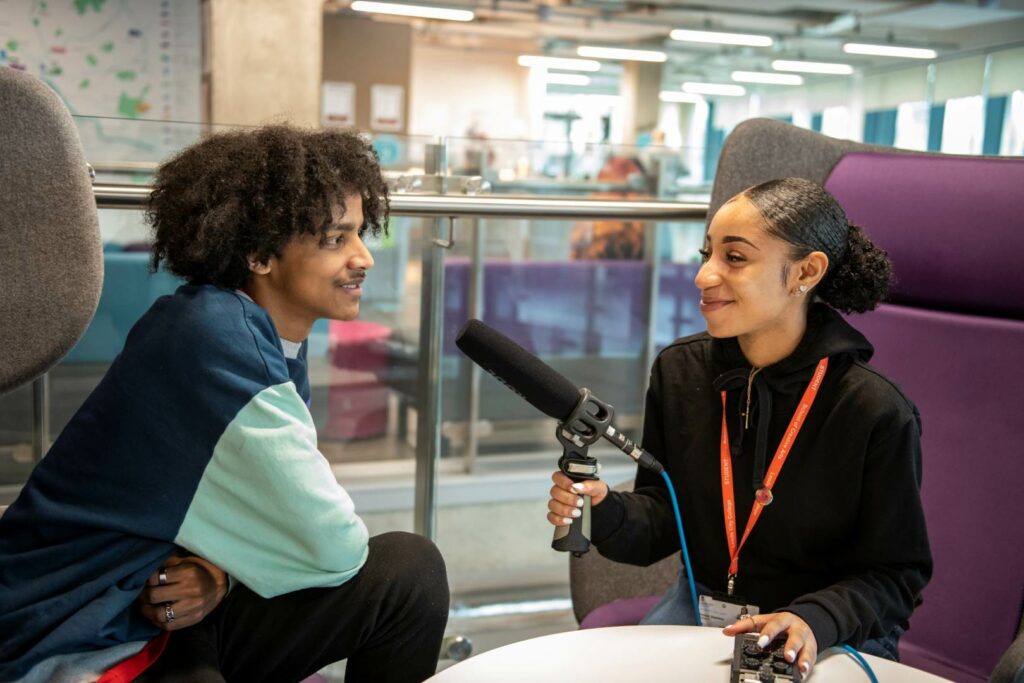 Two Journalism and Media students conducting an interview with one student holding the mic and recording equipment