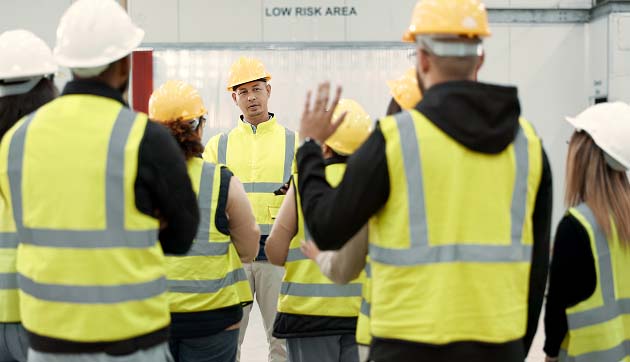 A group of people wearing high vis vests and safety helmets looking at the Safety Manager, one with a hand raised with a question