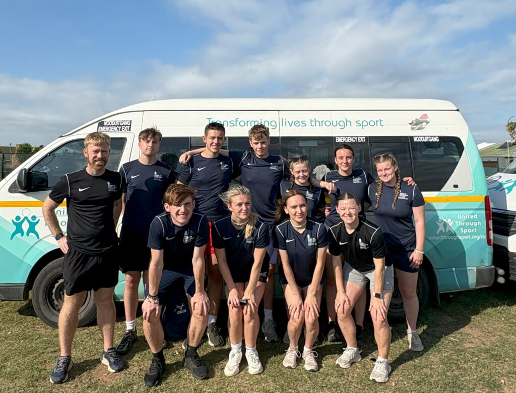Sports students from Leeds City College smiling beside their minibus during a coaching trip to South Africa